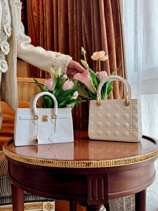 Scarlett Resin Handbag Vase and Victoria Resin Vase atop a gilded, round side table.