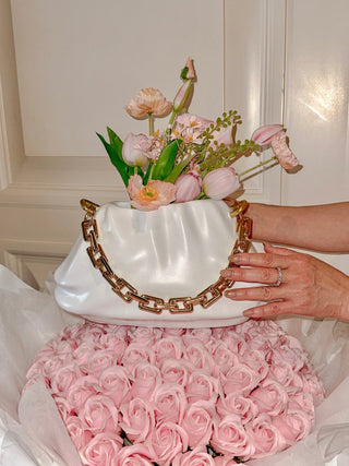 Sylvie Cloud Handbag with Gold Chain Resin Vase atop a massive pink rose bouquet.