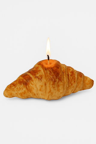 The French Croissant Candle with a lit flame, designed by Anaïs Candle.