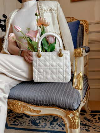 Woman gently touching a Scarlett Resin Handbag Vase on a gilded chair.