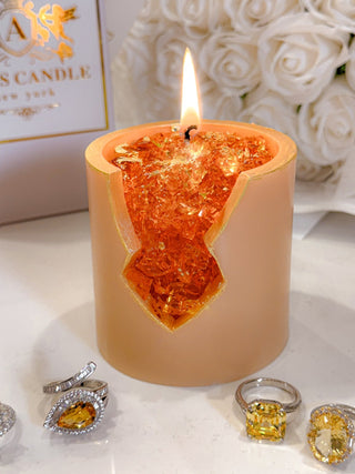 A warmly lit 18K Gold Citrine Crystal Candle – Prosperity & Success surrounded by jewelry.