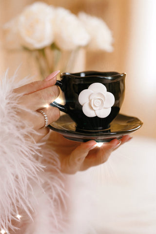 Black teacup with white floral design held by a hand against a blurred floral background