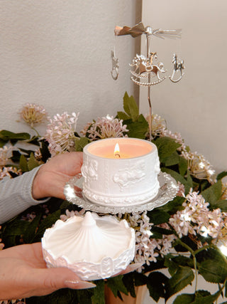 A woman holding a Starry Sky Carousel Candle in front of a floral backdrop.