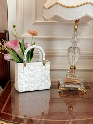Scarlett Resin Handbag Vase in Beige sat atop a wooden, gilded nightstand.
