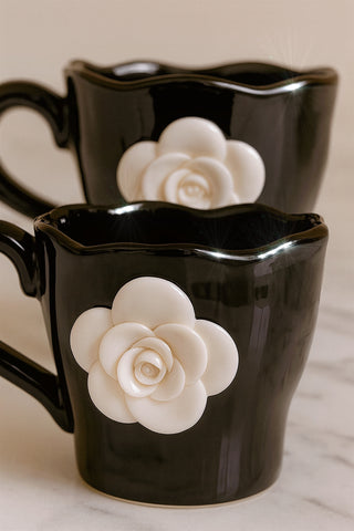 Two black mugs with white floral designs on a neutral background.