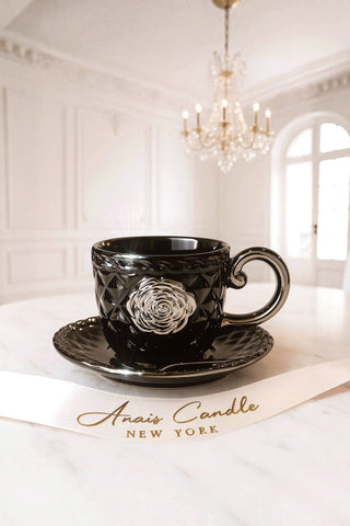 Black ceramic cup with floral design on a saucer in a elegant room with chandelier.