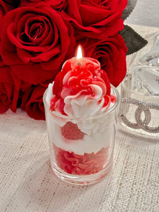 A Strawberries & Cream Candle with a lit flame, atop a white marble coffee table.