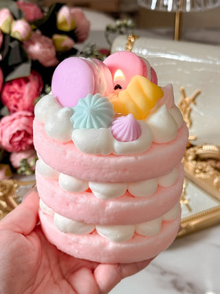 Dreamy Macarons & Cream Tart Candle held in hand with floral bouquet in background.
