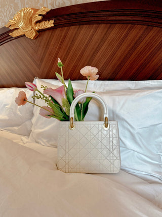 Scarlett Resin Handbag Vase in Beige atop a luxurious hotel bed.