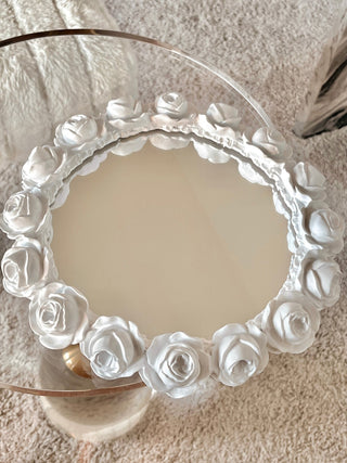A woman gently places the White Roses Mirror Tray down onto a luxurious bed.