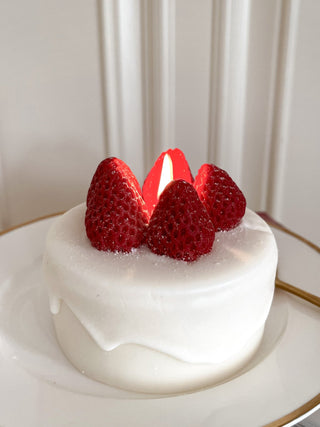 A lit Anaïs Strawberry Shortcake Candle on a gold rimmed plate.