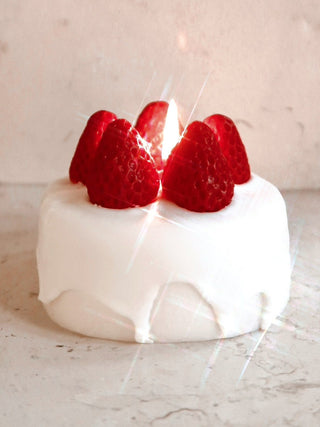 A lit Anaïs Strawberry Shortcake Candle made from premium beeswax and soy wax.