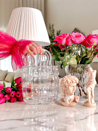 Camélia Padded Glass Handbag Vase in Rainbow set atop a marble dining table surrounded by pink flowers.