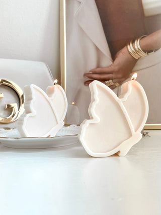 Two Dreamy Butterfly Candles on a gold plate with a luxury handbag in the background.