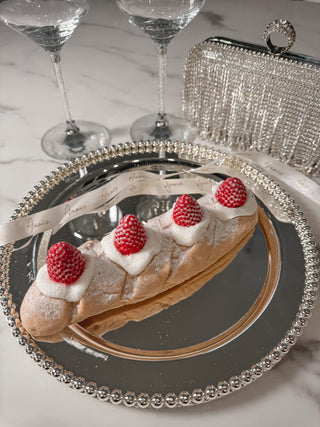 Strawberry & Cream Bread Candle atop a beautiful, elegant plate with tablecloth and wine glasses.