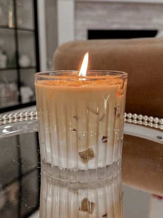 A lit Iced Caffè Candle on a reflective tray next to a plush brown couch..