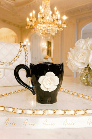 Black mug with a white flower design on a decorative table with a chandelier in the background
