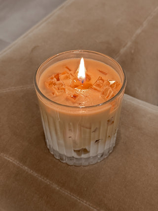 A lit Iced Caffè Candle atop a plush brown couch.