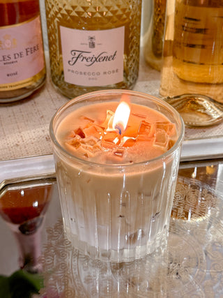 A lit Iced Caffè Candle on a marble table in front of several bottles of beautiful wine.
