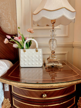Scarlett Resin Handbag Vase sat atop a wooden, gilded nightstand.