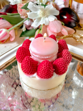 A lit Macaron & Strawberry Cake Candle next to a floral bouquet.