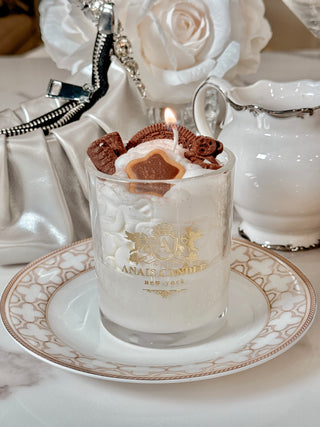 A lit Chocolate Bear & Cookies Latte Candle bearing our Anaïs Candle cupids and shield emblem.
