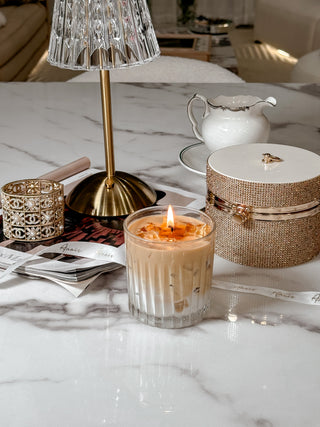 A lit Iced Caffè Candle on a beautiful marble dining table with a crystal and gold lamp..