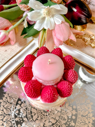 A lit Macaron & Strawberry Cake Candle on a reflective silver tray.