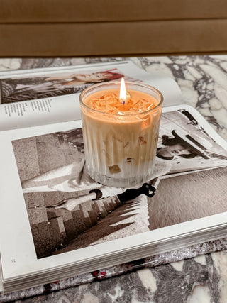A lit Iced Caffè Candle atop a haute magazine on a marble coffee table.
