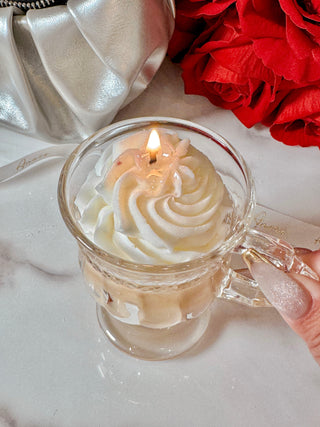 A lit Vanilla Ice Cream Latte Candle next to a luxurious clutch and red rose bouquet.