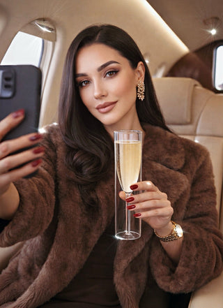 Woman in a luxurious vehicle holding a Maeve glass with champagne, taking a selfie.