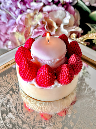 A lit Macaron & Strawberry Cake Candle on a reflective silver mirror tray next to a beautiful lampshade.