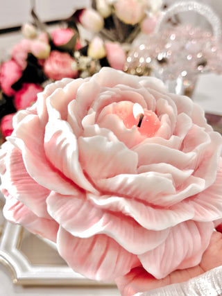 A lit Blooming Peony Candle - XXL surrounded by lavish flower bouquets.