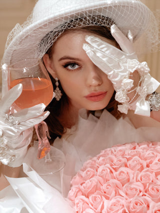 A woman wearing silky white gloves toasting a Cindarella’s Glass Slippers Wine Glass.