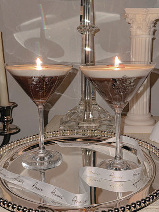 Two lit Lux Espresso Martini Candles surrounded by Anaïs Candle ribbon.