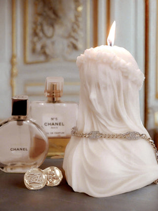 A lit 'Amour, Anaïs' candle next to perfume and jewelry.