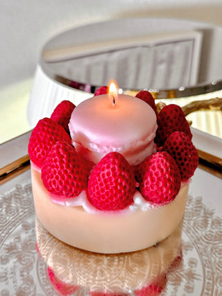 A lit Macaron & Strawberry Cake Candle on a reflective silver mirror tray.