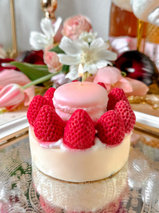 A lit Macaron & Strawberry Cake Candle next to a floral bouquet and reflective silver tray.
