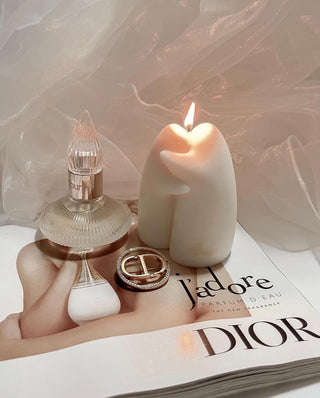 A lit Cuddle Ghosts Candle next to a luxurious perfume bottle.