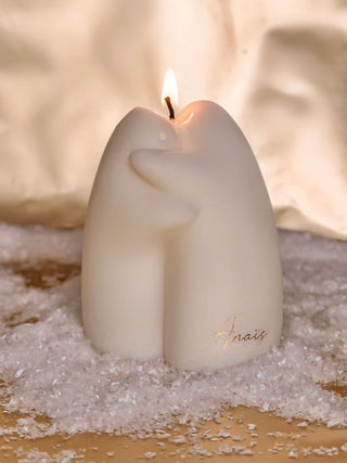 A lit Cuddle Ghosts Candle on shiny snowflakes.