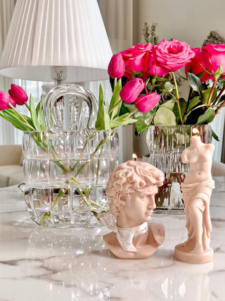Camélia Padded Glass Handbag Vase in Rainbow with decorated with pink tulips next to an Anaïs Man and Venus in French Rose Pink candle.