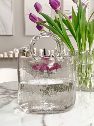 Olivia Glass Handbag Vase atop a marble dining table with a background of Anaïs candles.